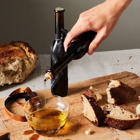 Mano versa vino da bottiglia su tagliere con pane, olio e fette di pane.